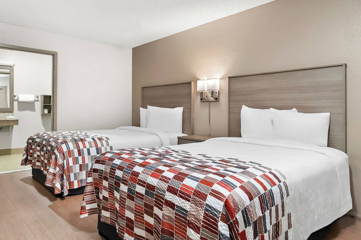 Habitación de hotel con dos camas, cada una con colcha acolchada, mesita de noche, lámpara de pared y espejo.