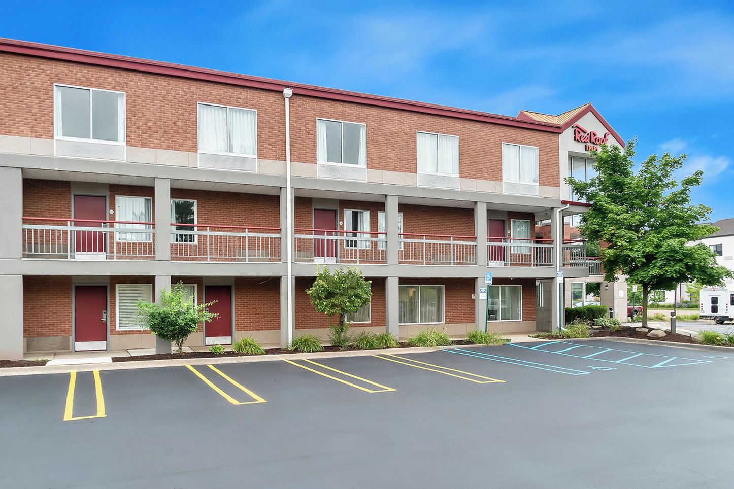 A Red Roof Inn with a two-story brick building, a parking lot with marked spaces, and a small tree in the foreground.