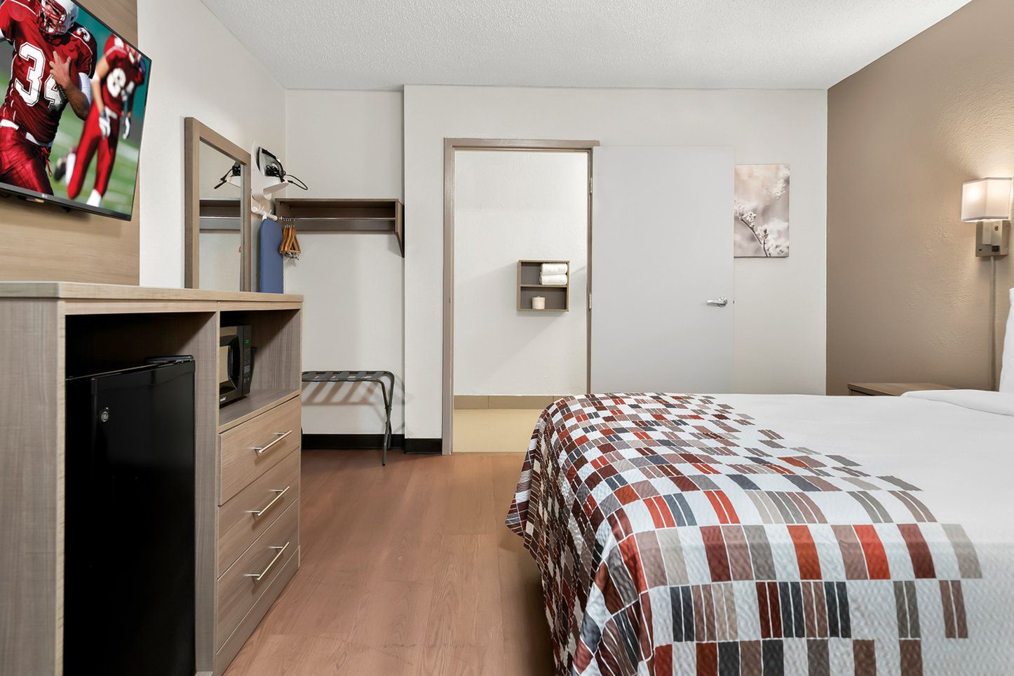 Habitación de hotel con cama, escritorio con computadora, microondas, armario y puerta que da a otra habitación.