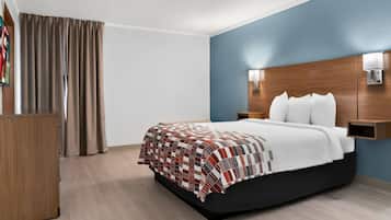 A hotel room with a bed, a wooden nightstand, a desk, and a blue accent wall.