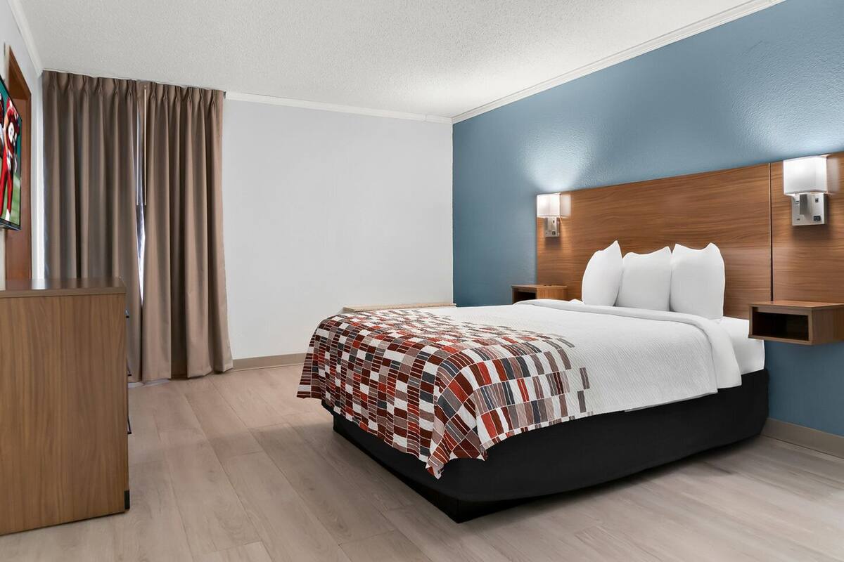 Habitación de hotel con una cama, una mesita de noche de madera, un escritorio y una pared azul decorativa.