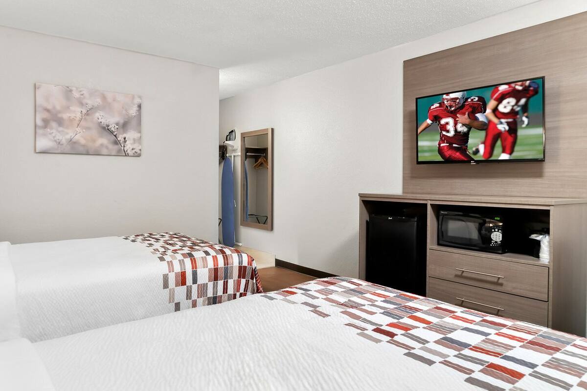 Habitación de hotel con dos camas, televisión, microondas y refrigerador pequeño.