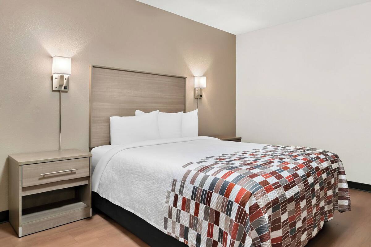 Una habitación de hotel con cama, mesitas de noche y lámparas de pared.