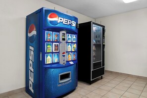 A blue Pepsi vending machine with various drink options and a black refrigerator next to it. - Red Roof Inn Auburn Hills (Auburn Hills)