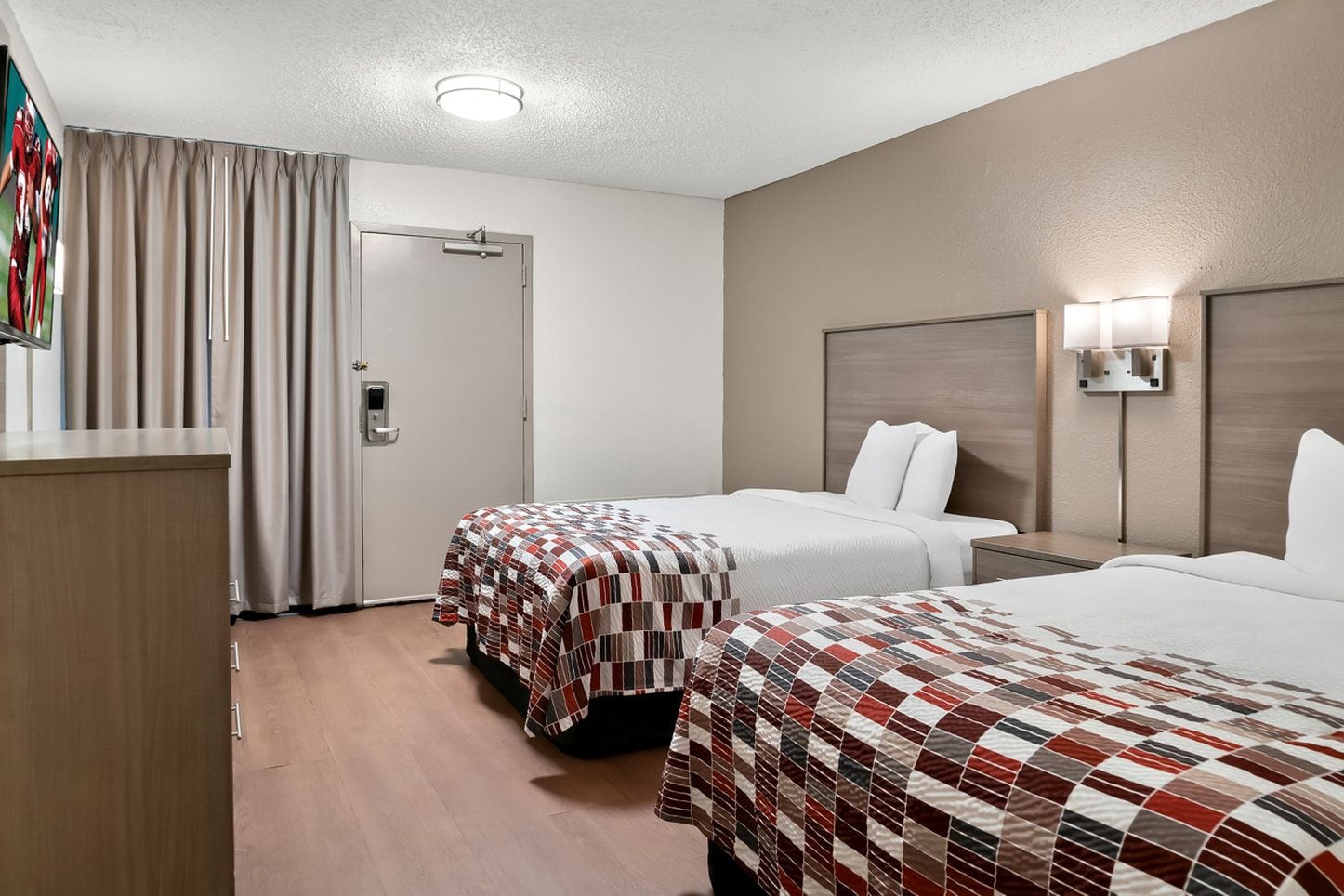 Une chambre d’hôtel avec deux lits, un bureau, une porte et une lampe fixée au mur.