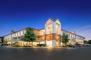 A hotel with a central tower featuring a sign, multiple balconies, and a parking lot. - Red Roof Inn Auburn Hills (Auburn Hills)