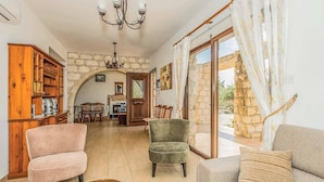 A cozy living room with a stone archway, a wooden bookshelf, and a view through a glass door. - Villa Aphrodite Argaka (Argaka)