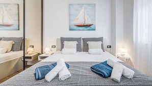 Ein Hotelzimmer mit einem Bett, zwei Nachttischen mit Lampen, einem großen Spiegel und zwei Bildern von Segelbooten an der Wand.
