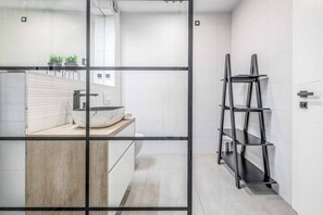 Ein modernes Badezimmer mit Marmorwaschbecken, einem Holzwaschtisch und einem schwarzen Metallregal.