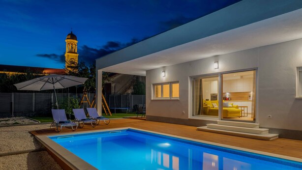 Ein modernes Haus mit Swimmingpool, Sitzgelegenheiten im Freien und Essbereich.
