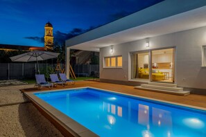 Ein modernes Haus mit Swimmingpool, Sitzgelegenheiten im Freien und Essbereich.