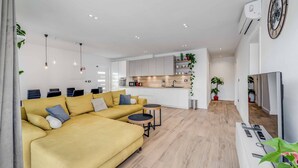 Ein modernes Wohnzimmer mit einem gelben Sofa, einem kleinen Couchtisch und einer TV-Konsole mit Fernbedienungen.