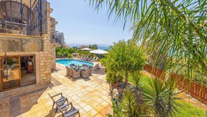 Uma área de piscina com espreguiçadeiras e uma mesa, cercada por paredes de pedra e vista para o mar.