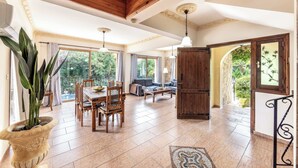 A spacious living area with a wooden ceiling, large windows, and a dining table with chairs. - Villa Sweet Memories (Argaka)