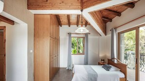 A bedroom with a wooden ceiling, a bed with a white bedspread, a nightstand, and a window with curtains. - Villa Sweet Memories (Argaka)