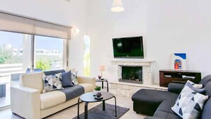 A modern living room with a sofa, a coffee table, a fireplace, and a TV mounted on the wall. - Sea Breeze Hideaway - Three Bedroom Villa, Sleeps 6 (Latchi)