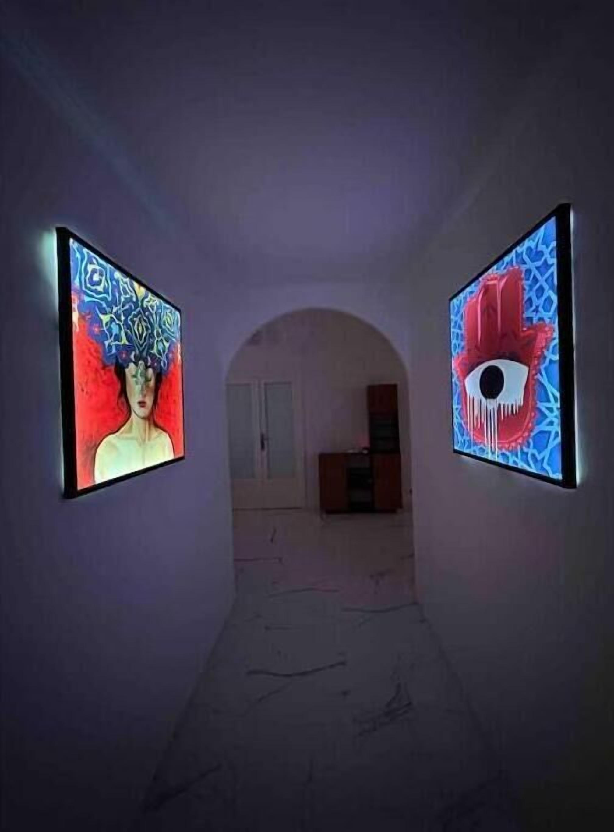 A hallway with two illuminated artworks on either side, leading to a room with a door and a cabinet.