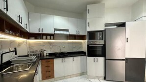 Una cocina moderna con armarios blancos, un refrigerador de acero inoxidable, un horno empotrado y un microondas.