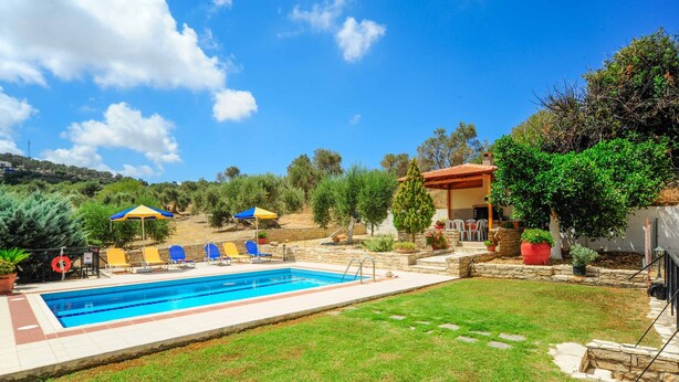A swimming pool with lounge chairs and umbrellas, surrounded by a well-maintained lawn and stone walls.