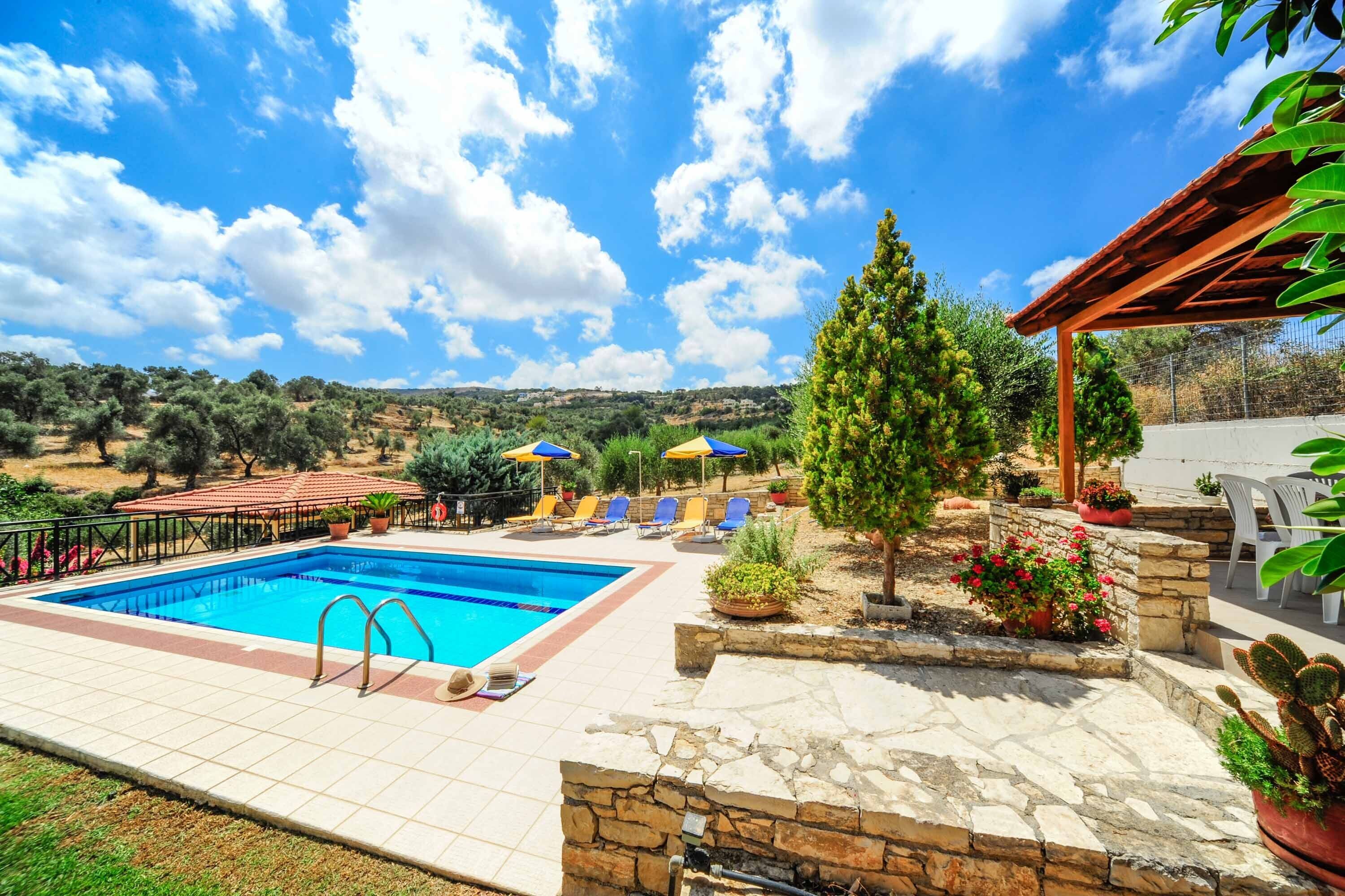 A swimming pool with lounge chairs and umbrellas, surrounded by stone walls and potted plants.