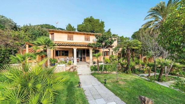 A two-story house with a tiled roof, a stone pathway leading to the entrance, and a well-maintained garden with palm trees and shrubs. - Ca na Tonina - Five Bedroom Villa, Sleeps 10 (Pollença)