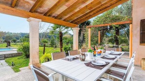 An outdoor patio with a white table set for dining, surrounded by chairs, and a pergola overhead. - Ca na Tonina - Five Bedroom Villa, Sleeps 10 (Pollença)