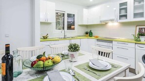 A modern kitchen with white cabinets, a green countertop, and a dining area with a table set for two. - Ca na Tonina - Five Bedroom Villa, Sleeps 10 (Pollença)