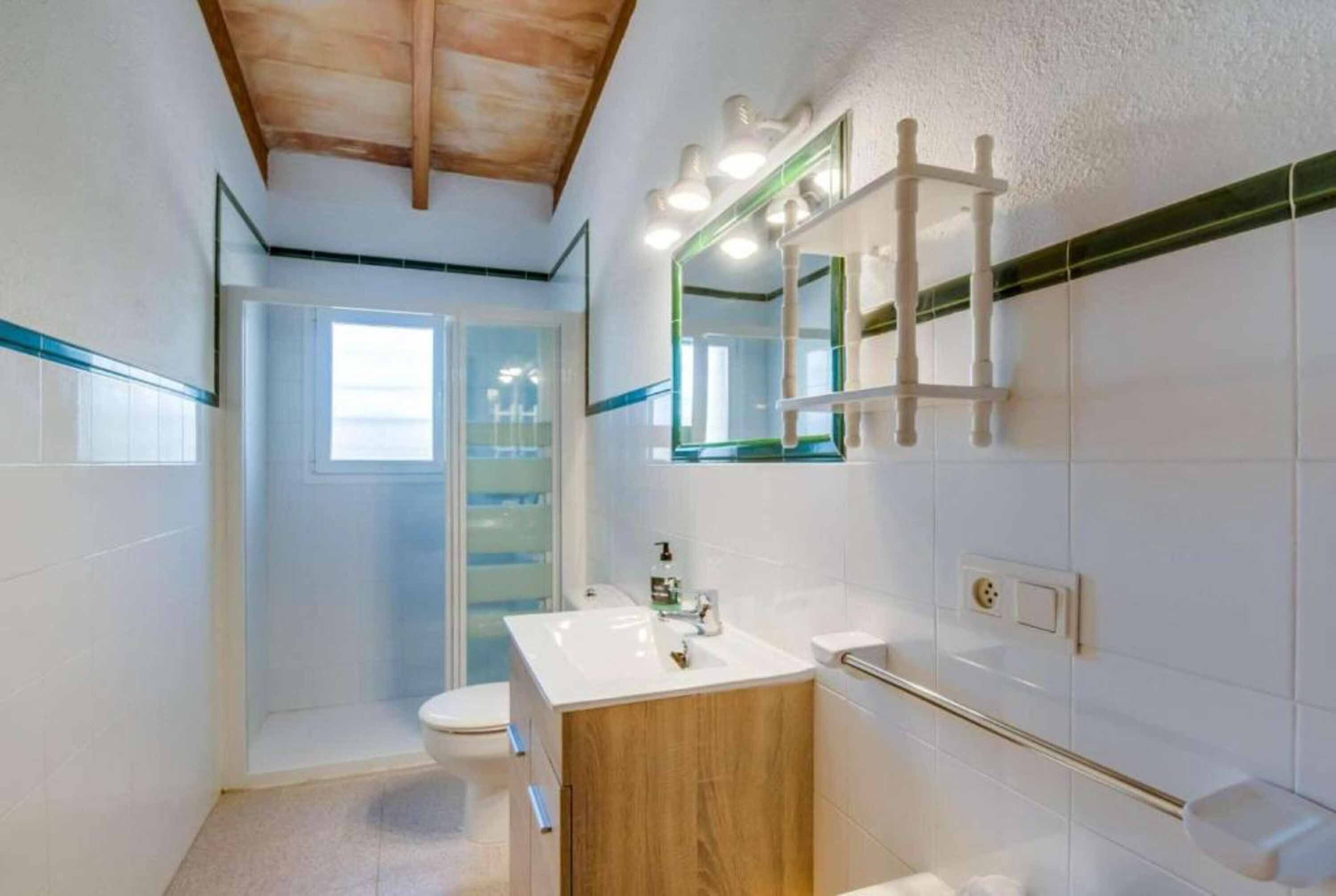 Ein Badezimmer mit Holzboden, weißen Fliesen, einem Waschbecken, einem Spiegel und einer Duschkabine.