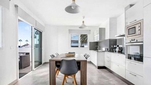 Une cuisine moderne avec des meubles blancs, une table à manger avec des chaises et des appareils électroménagers intégrés.