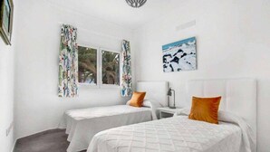 Une chambre avec deux lits, une fenêtre avec des rideaux, une table de chevet et un tableau au mur.
