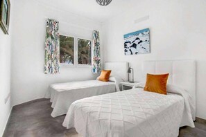 Ein Zimmer mit zwei Betten, einem Fenster mit Vorhängen, einem Nachttisch und einem Bild an der Wand.