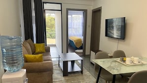 Une chambre d’hôtel moderne équipée d’un canapé, d’une table basse, d’une table à manger avec des chaises, d’un téléviseur et d’un distributeur d’eau.
