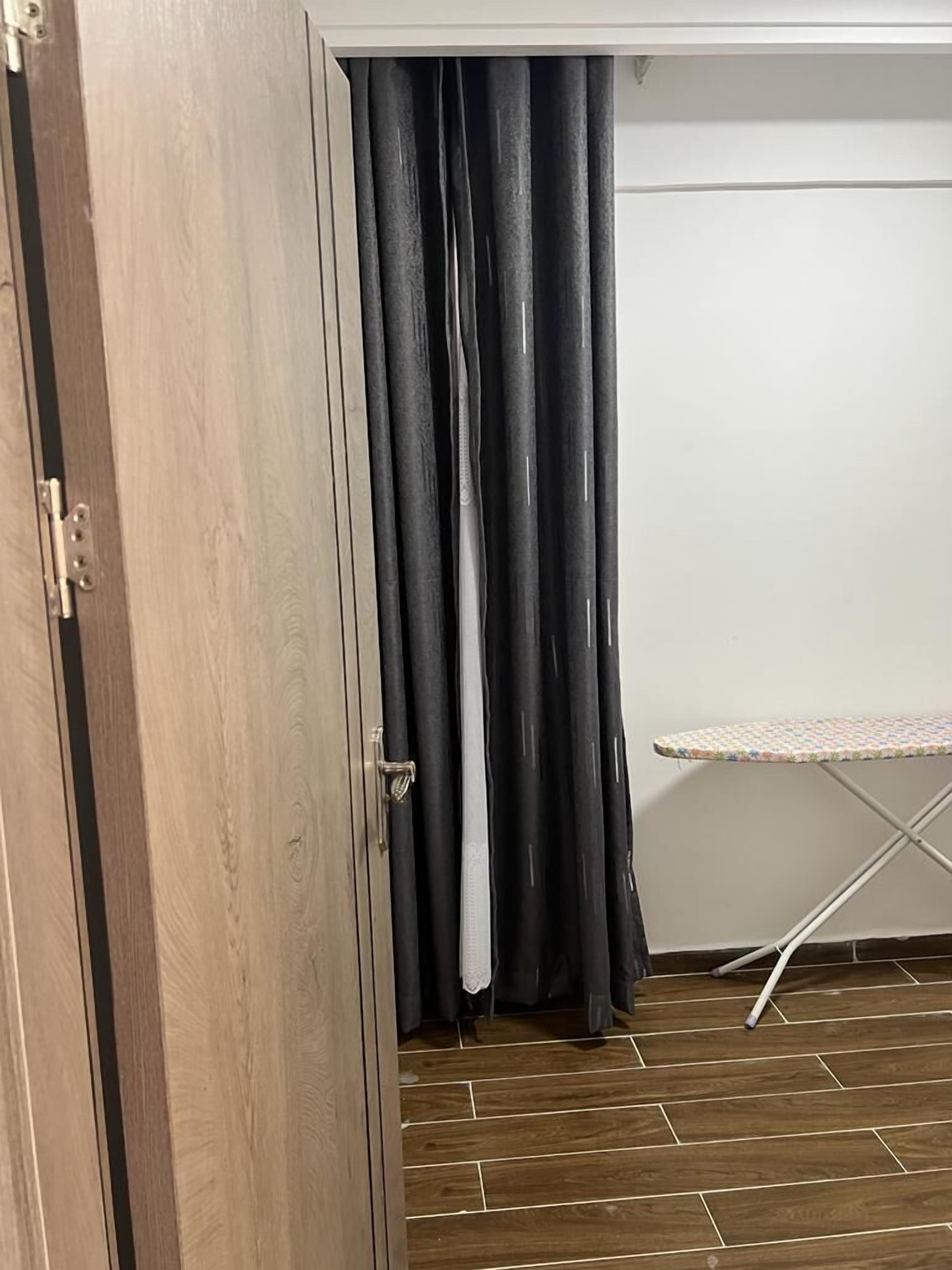 A room with a wooden door, black curtains, and a white ironing board.