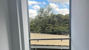 Une pièce dotée d’une grande fenêtre donnant sur un bâtiment dont le toit est fait de tôles ondulées et un des murs est en briques. On y trouve deux chaises grises.