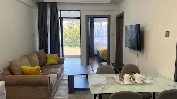 Une chambre d’hôtel moderne équipée d’un canapé, d’une table à manger avec des chaises, d’un téléviseur à écran plat fixé au mur et d’un balcon avec une porte coulissante.