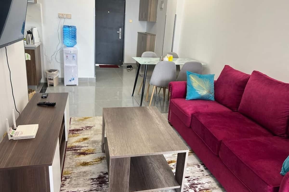 A modern living room with a red sofa, a coffee table, and a TV stand. There is a dining area with a table and chairs in the background.