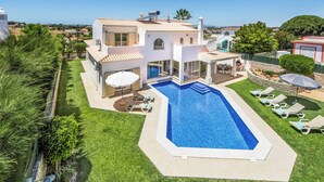 Une grande maison avec une piscine, un patio doté de chaises longues et une pelouse bien entretenue.