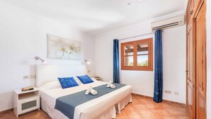 A bedroom with a double bed, a nightstand, a bedside table, a window with curtains, and an air conditioning unit. - Villa Vobis - Three Bedroom Villa, Sleeps 6 (Mallorca)