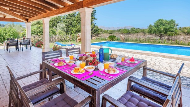A covered outdoor dining area with a pool view, wooden furniture, and a breakfast setup. - Villa Vobis - Three Bedroom Villa, Sleeps 6 (Mallorca)