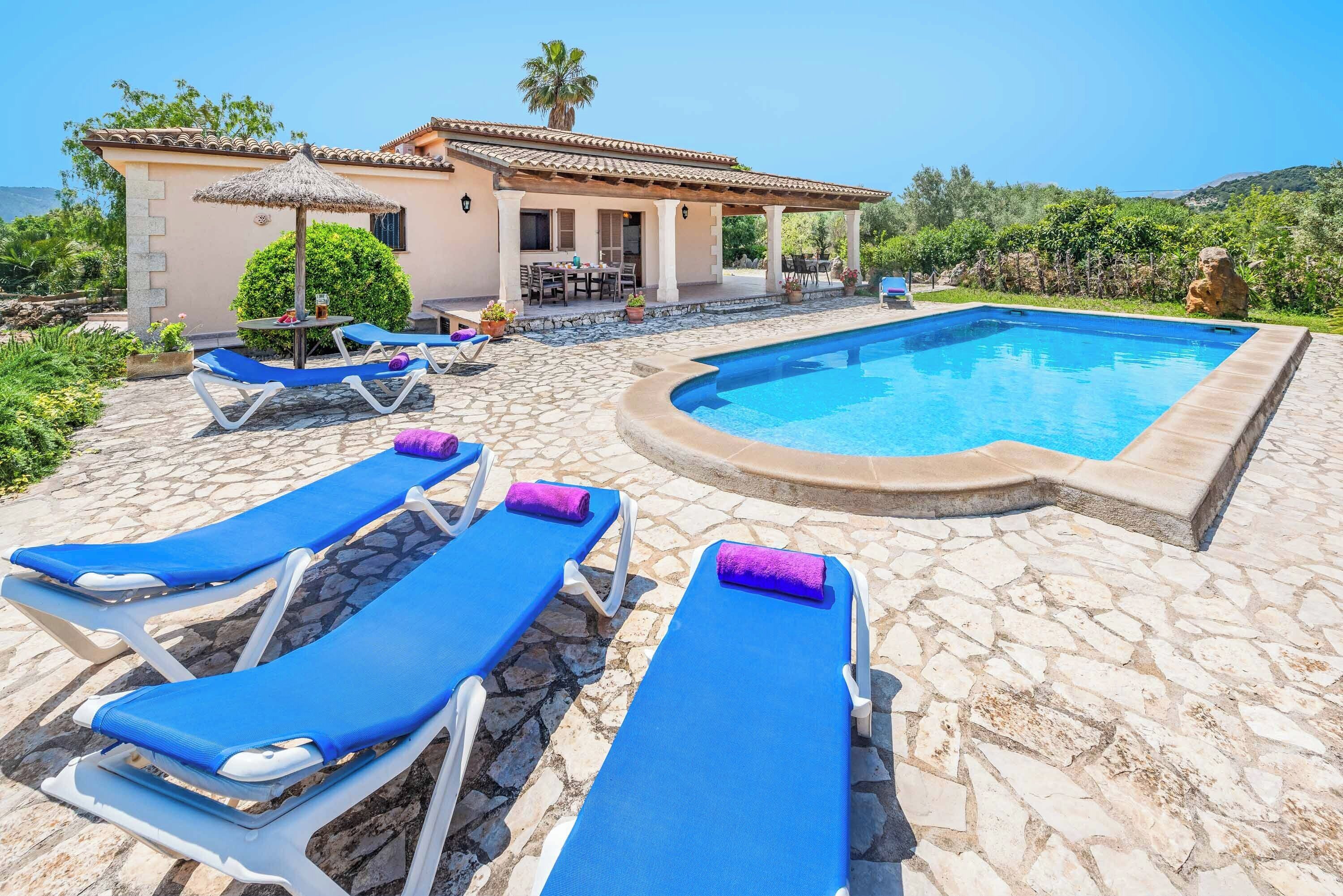 A pool area with lounge chairs and a house in the background.