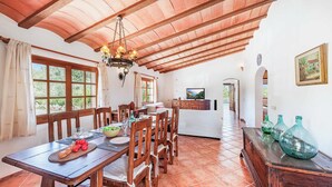 A dining area with a wooden table set for six, surrounded by chairs. A chandelier hangs from the ceiling, and there is a television in the background. - Villa Vobis - Three Bedroom Villa, Sleeps 6 (Mallorca)