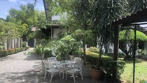 Une terrasse avec une table ronde et des chaises, entourée de plantes en pot et d’arbres.