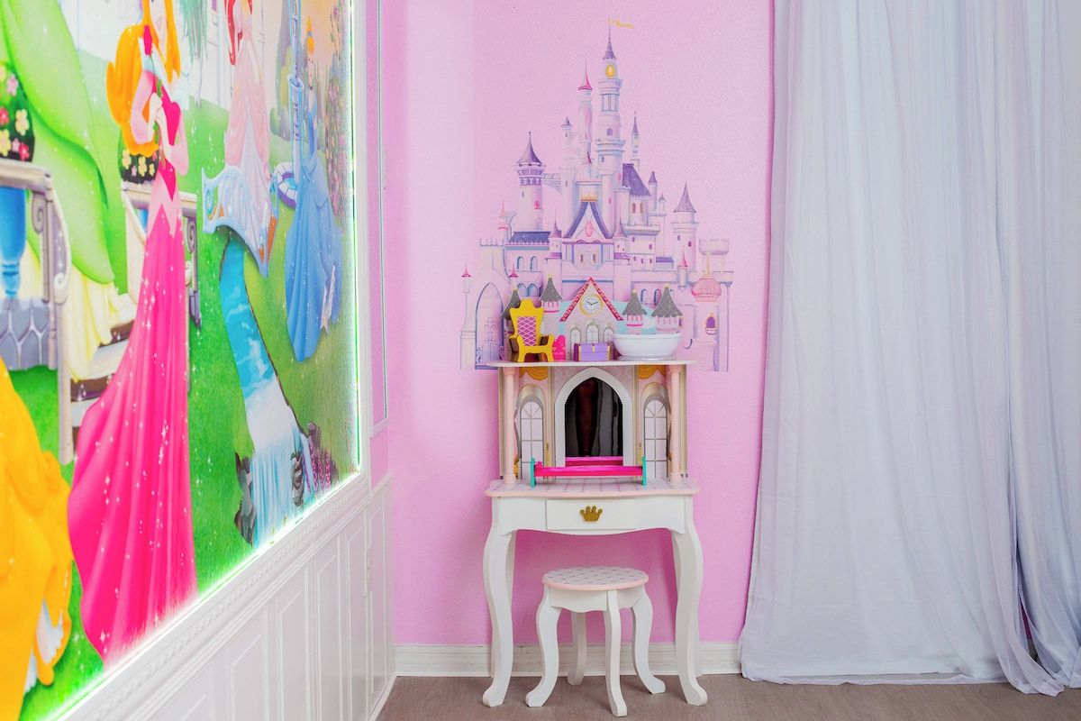 Een kamer met een roze muur, een wit bureau met een klein krukje, en een muurschildering van een kasteel.