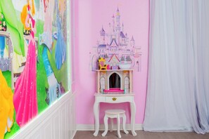 Una habitación con pared rosa, un escritorio blanco con un taburete pequeño y un mural con motivos de castillo.