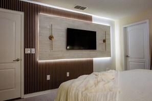 A hotel room with a large bed, a mounted TV, and a wall with vertical wooden slats. - 8952 Private Pool Townhome Near Disney - Paradise Palms (Kissimmee)