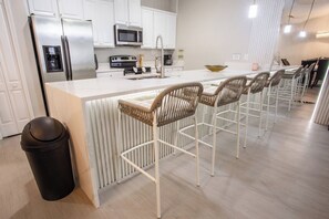 Une cuisine moderne avec des meubles blancs, des appareils en acier inoxydable et un îlot central doté de tabourets de bar.