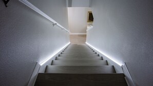 Eine Treppe mit Holzstufen und weißen Wänden, die zu einer Zwischenebene mit einem gerahmten Bild führt.