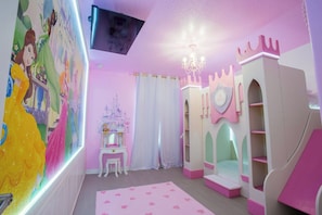 Une salle de jeux pour enfants avec une cabane à jouer sur le thème d’un château, une coiffeuse avec un miroir et un mur orné d’une fresque représentant une princesse.