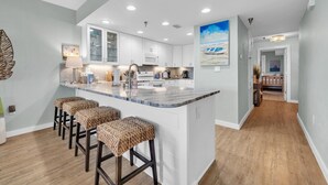 Una cocina moderna con gabinetes blancos, una isla de mármol con taburetes y luces empotradas en el techo.