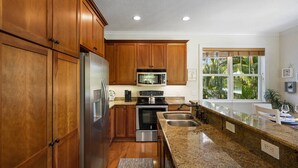 Une cuisine moderne dot ée de meubles en bois, d’appareils électroménagers en acier inoxydable, de plans de travail en granit et d’une grande fenêtre offrant une vue sur la verdure.